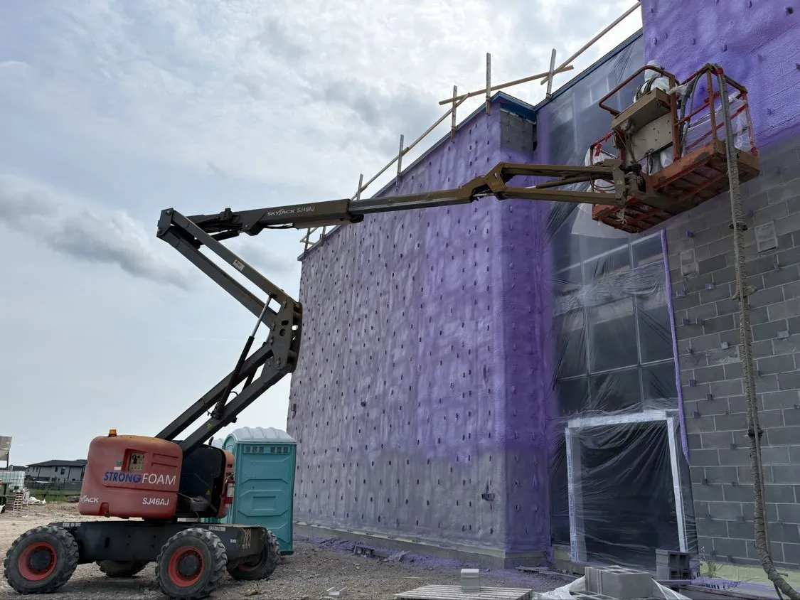 Strong Foam boom lift spraying exterior foam insulation on a large masonry wall