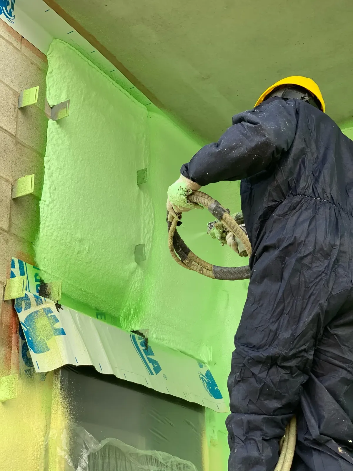 Installer in protective coveralls and respirator applying spray foam