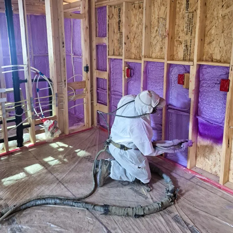 Installer in protective suit applying spray foam insulation to wood-frame walls